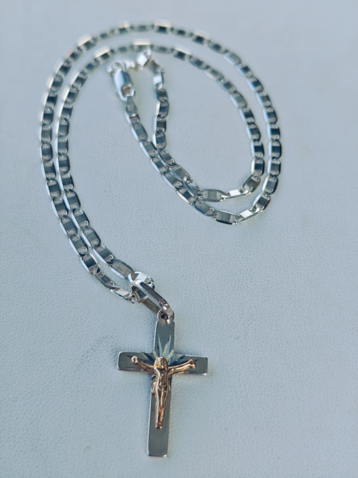 Cadena con cruz fotografiada sobre una superficie clara